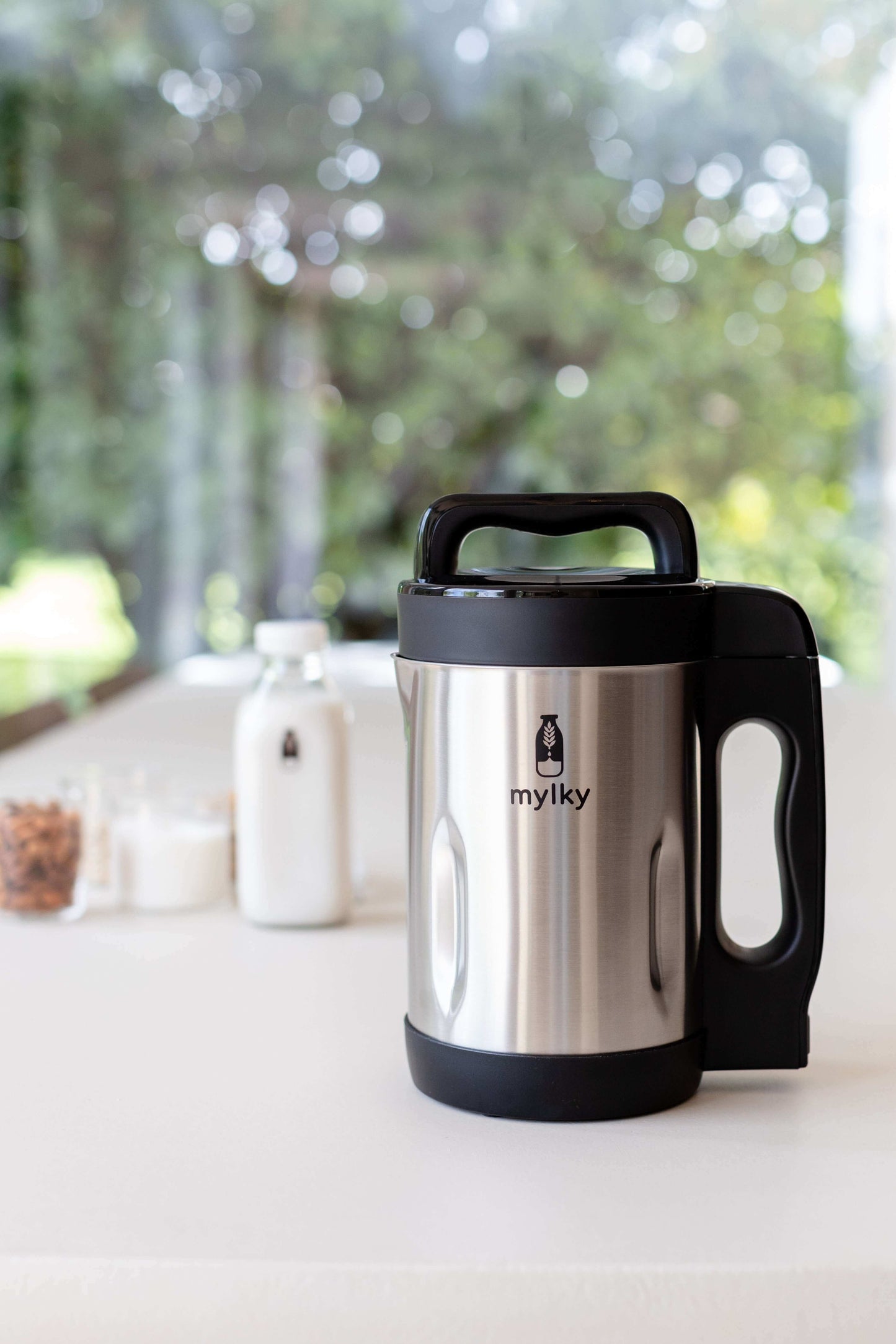 Mylky stainless steel plant-based milk maker on a kitchen counter with bottles and ingredients